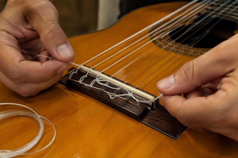 Mãos amarrando uma corda nova de nylon no cavalete de um violão