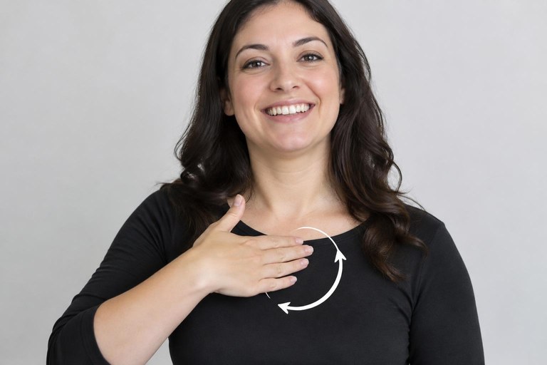 A signer brushing a flat hand upward on the chest for the sign HAPPY with a smiling face