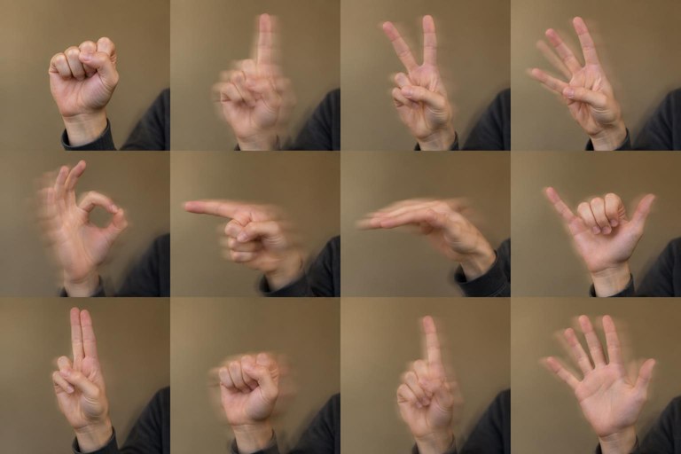 A hand fingerspelling at shoulder height with slight motion blur showing smooth movement between letters