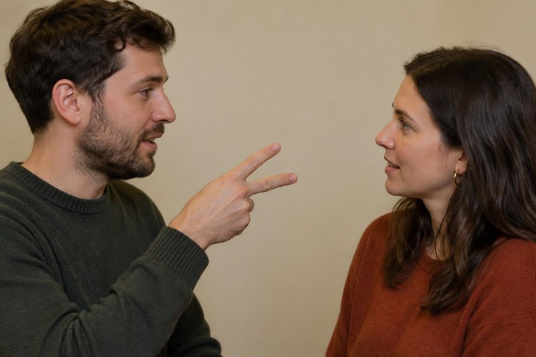 A signer forms the two-of-us pronoun with a sideways V hand between two people