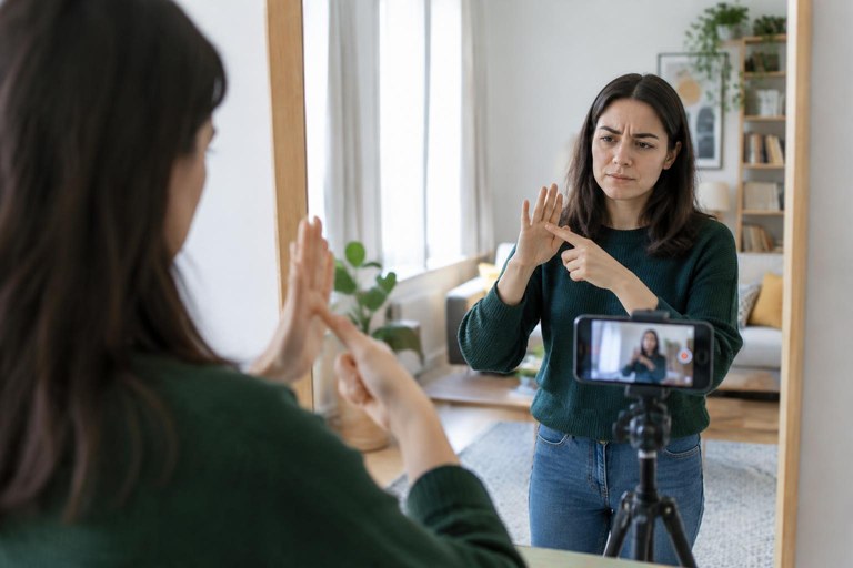 A learner practising question signs in front of a mirror while recording on a phone